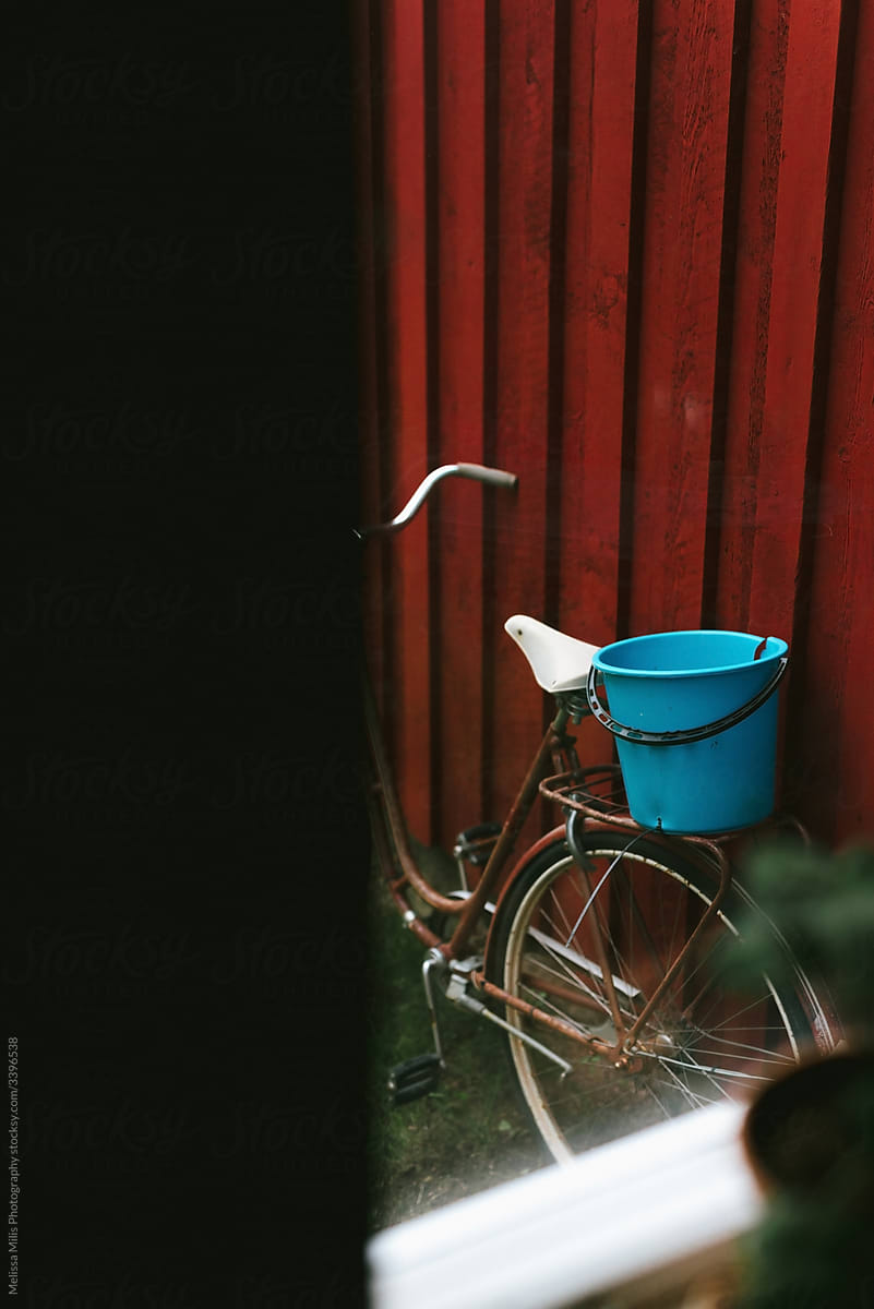old bike with blue bucket against a swedish wooden red house
