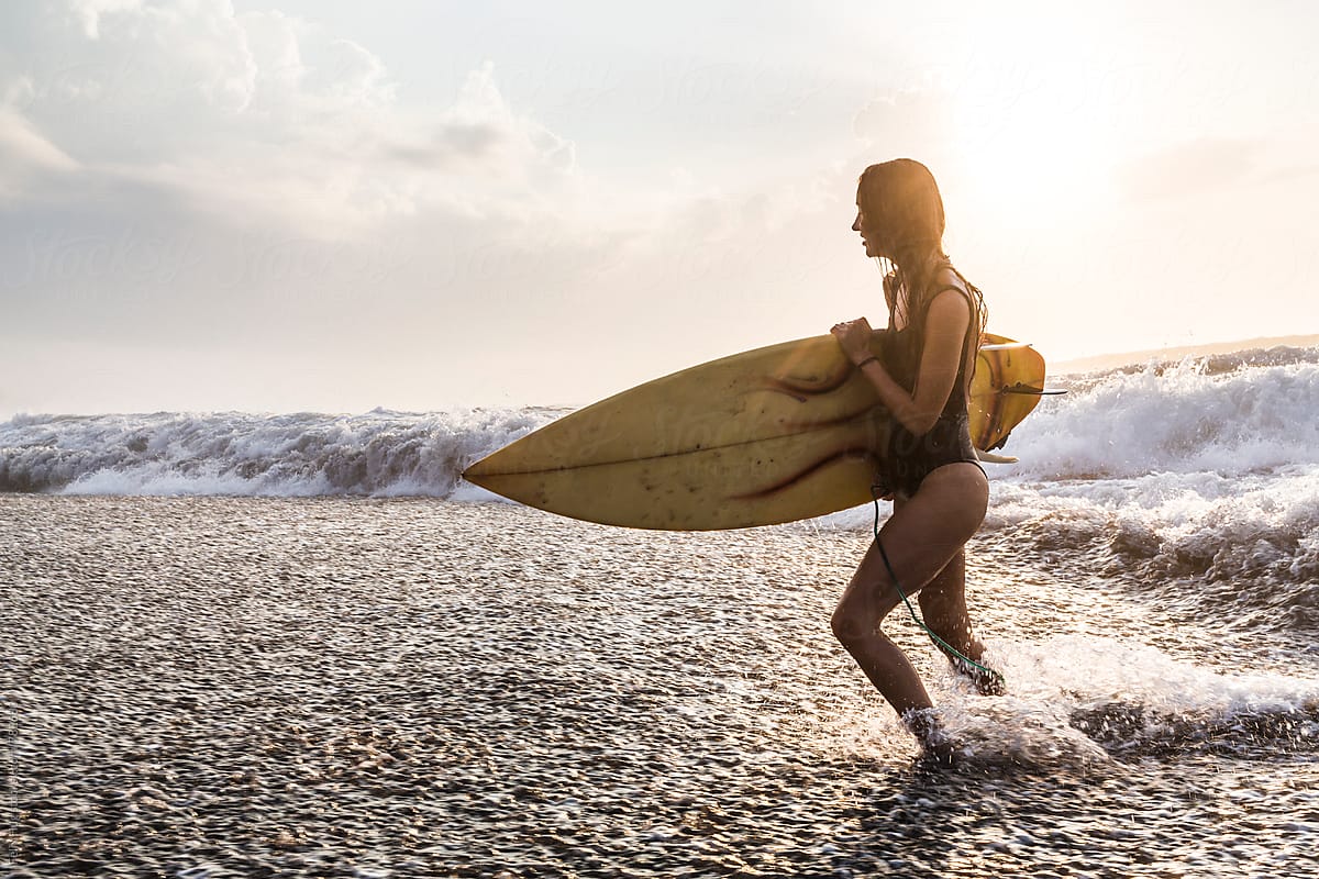 Woman running out of the water with surfboard