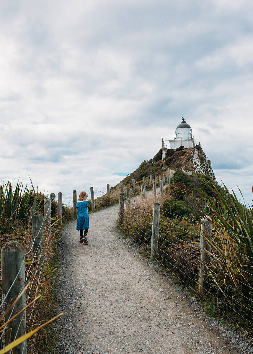 Young girl walking on a path towards a lighthouse