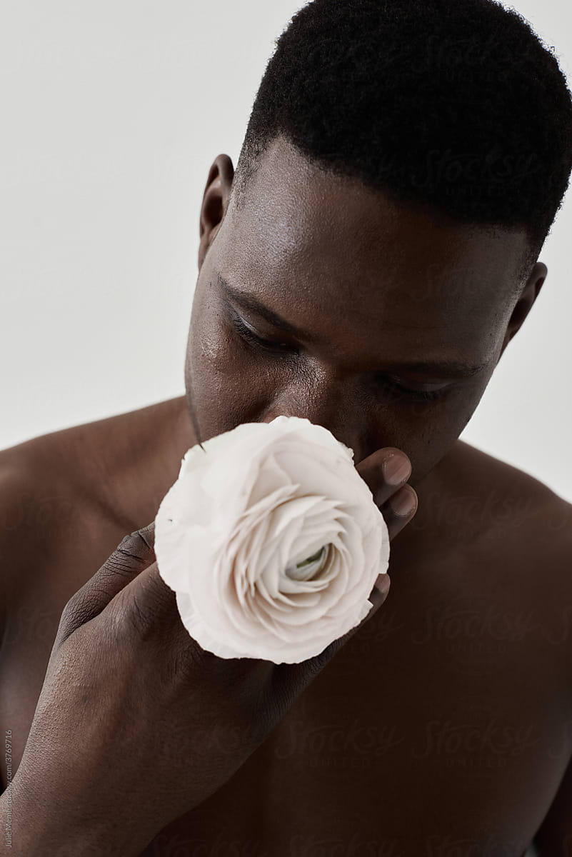 Closeup portrait of a topless african guy with a pale flower covered his mouth