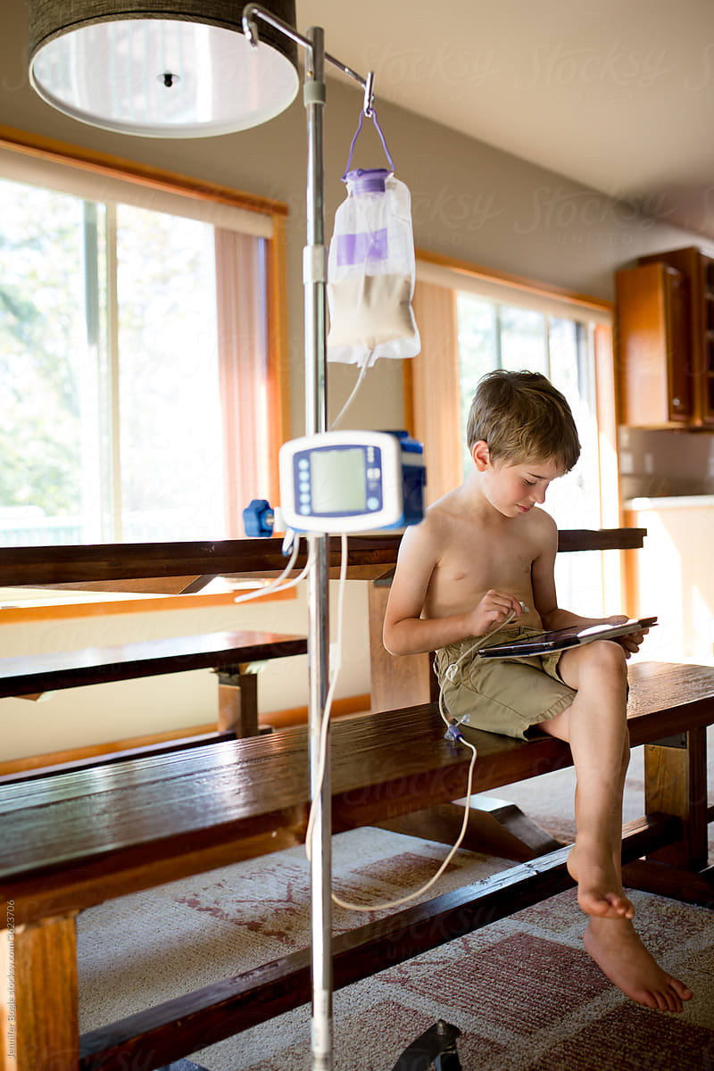 Boy reads on tablet while pump feeds him through g-tube