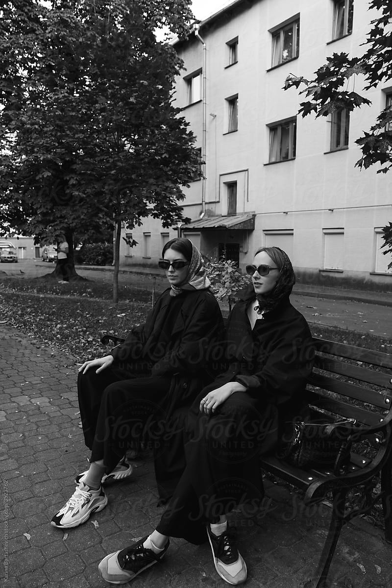 Stylish girls in coats and glasses sit on the bench