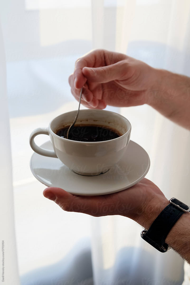 Crop faceless man stirring black hot coffee in cup