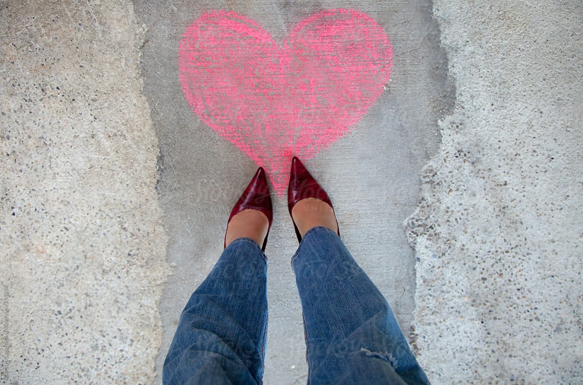 Woman in red heels and jeans standing over a pink chalk heart