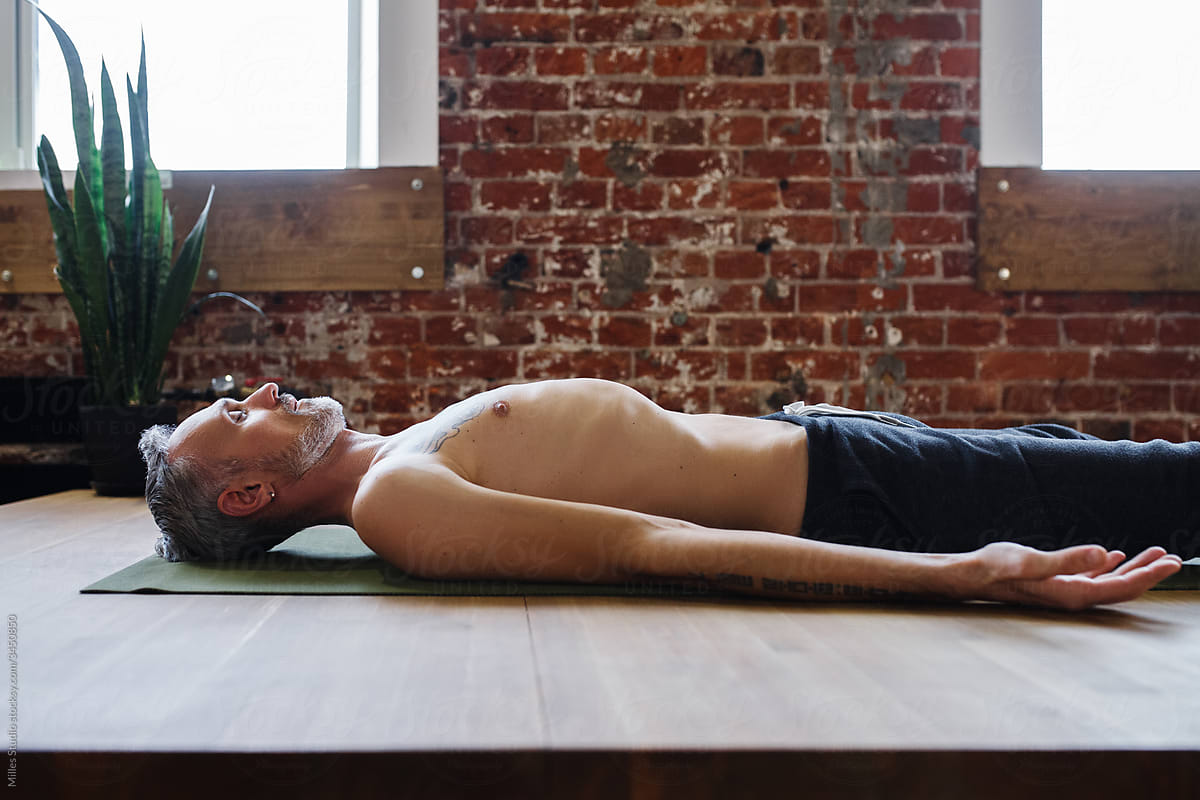 Relaxed middle aged man meditating in Savasana pose