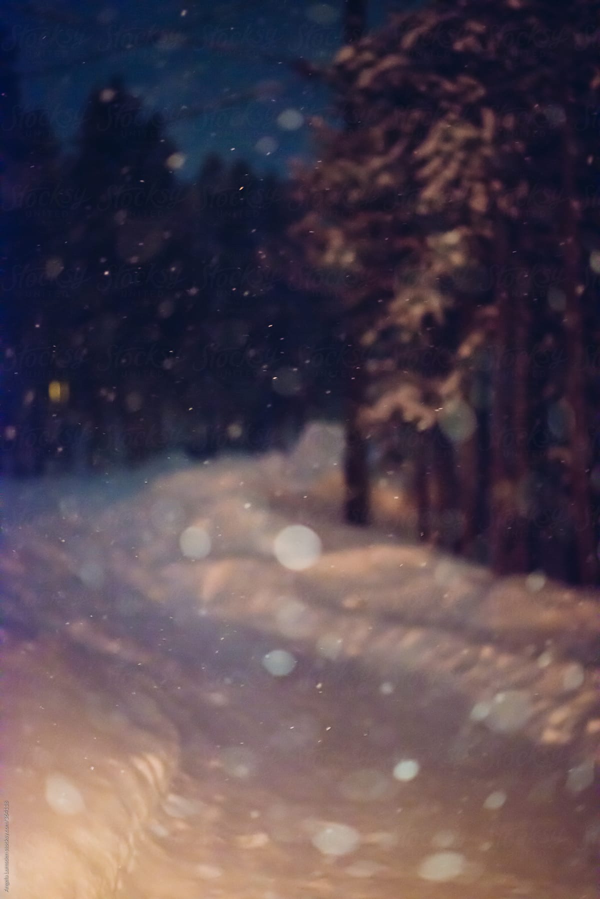 Defocused image of snow falling on a snow covered driveway at night