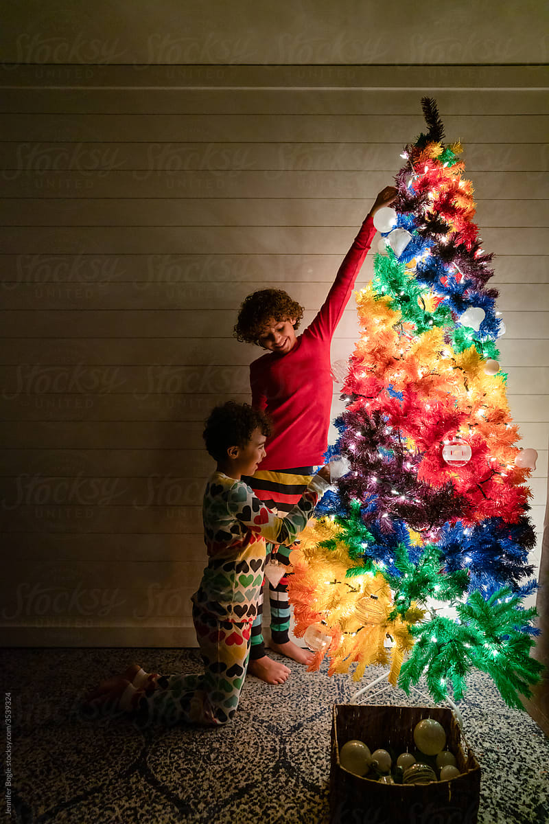 Laughing siblings decorate rainbow Christmas tree