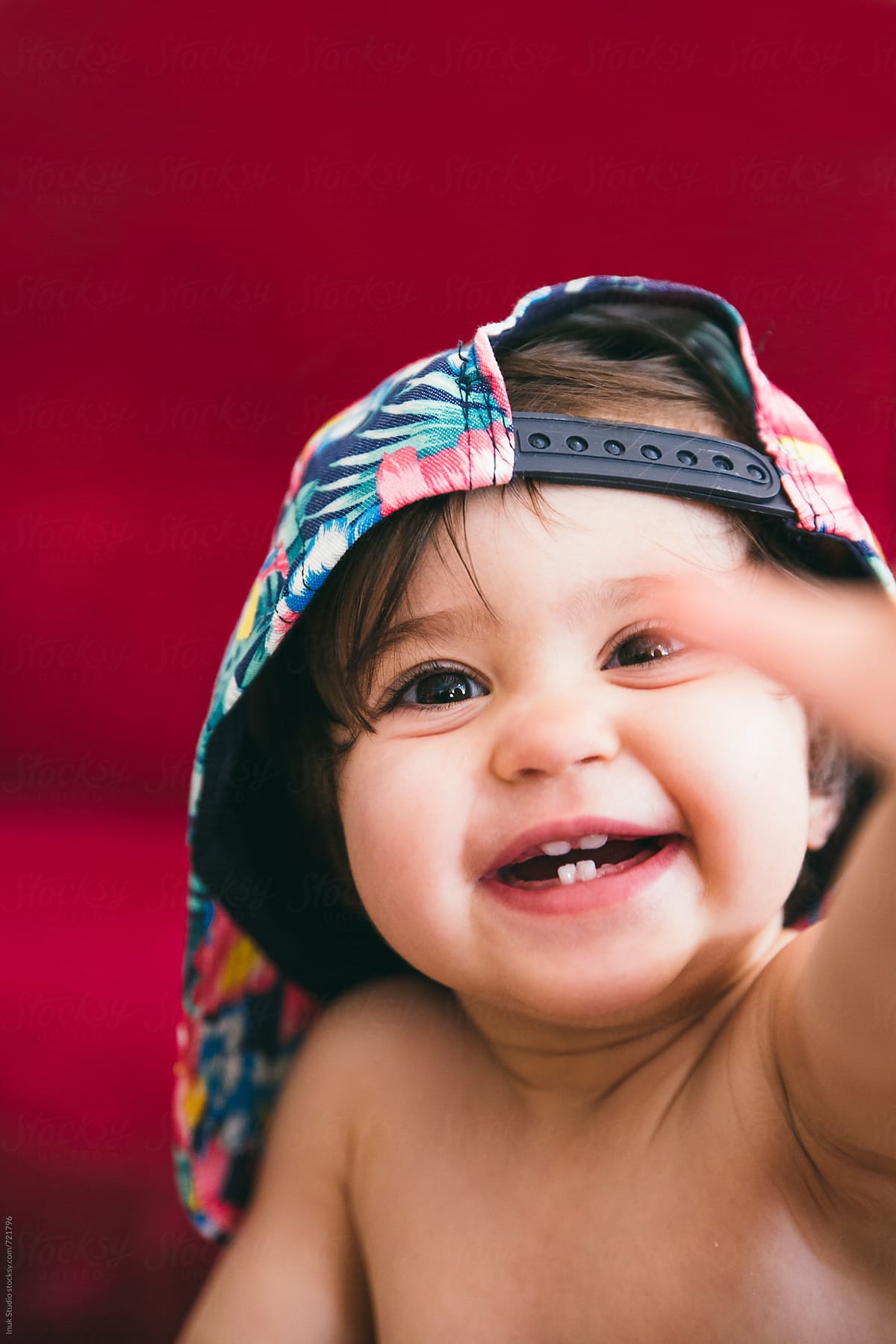 Stylish baby wearing a colourful flower cap smiling and trying to grab the camera