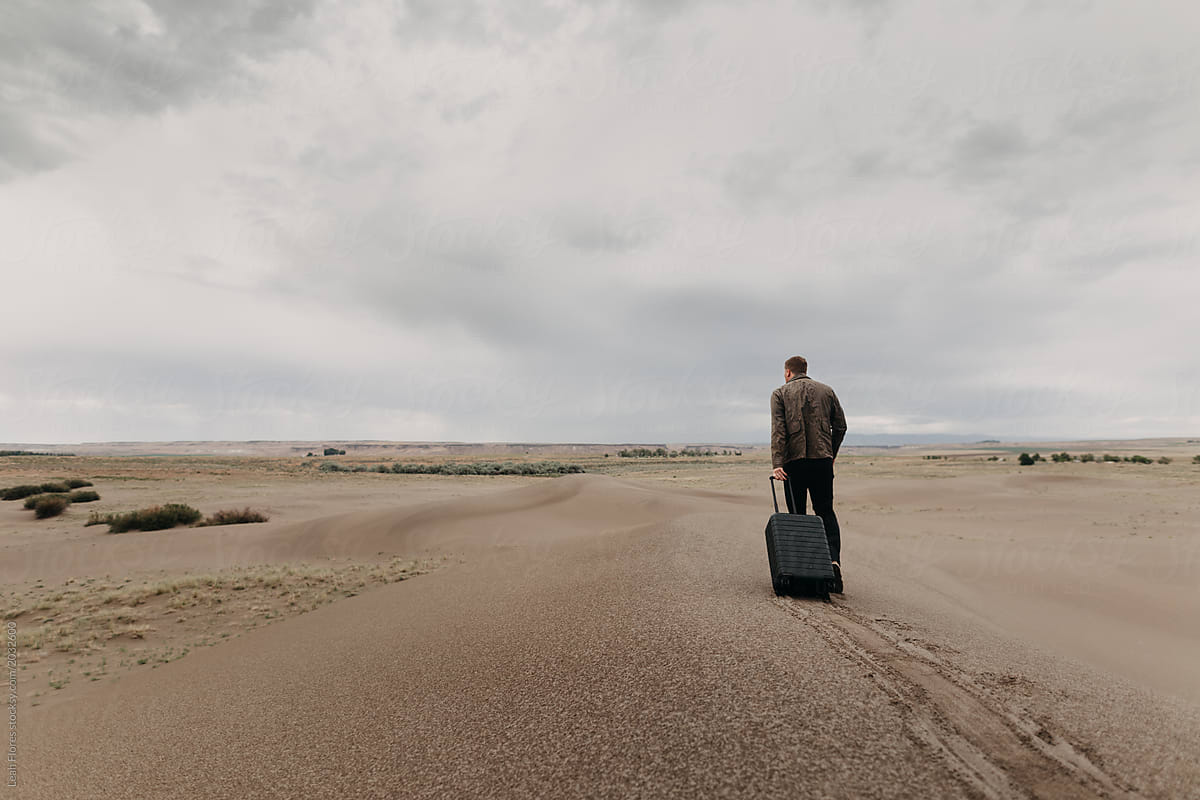 Man Walking Through Dunes Dragging Luggage