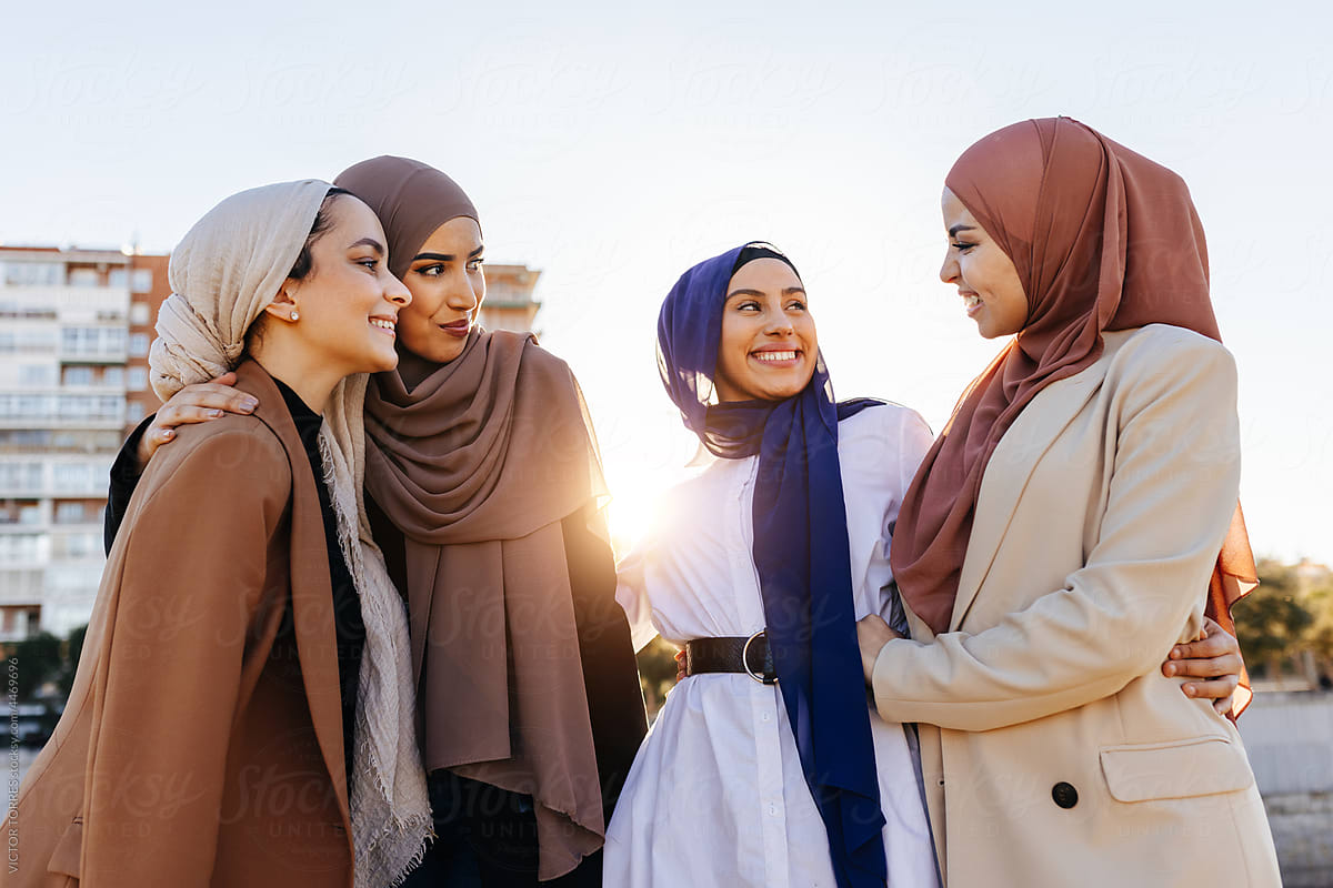Cheerful Muslim women in hijab talking to each other in city