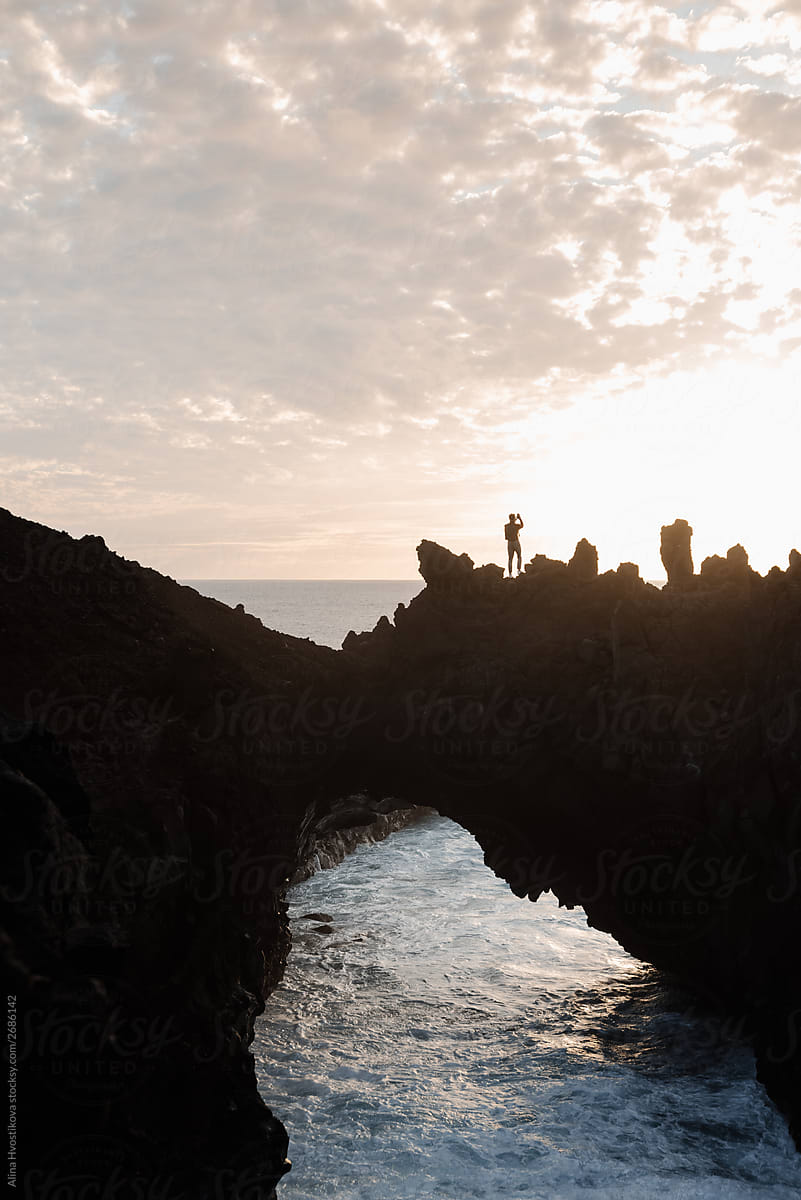 Silhouette of male on top of rocky bridge over ocean.