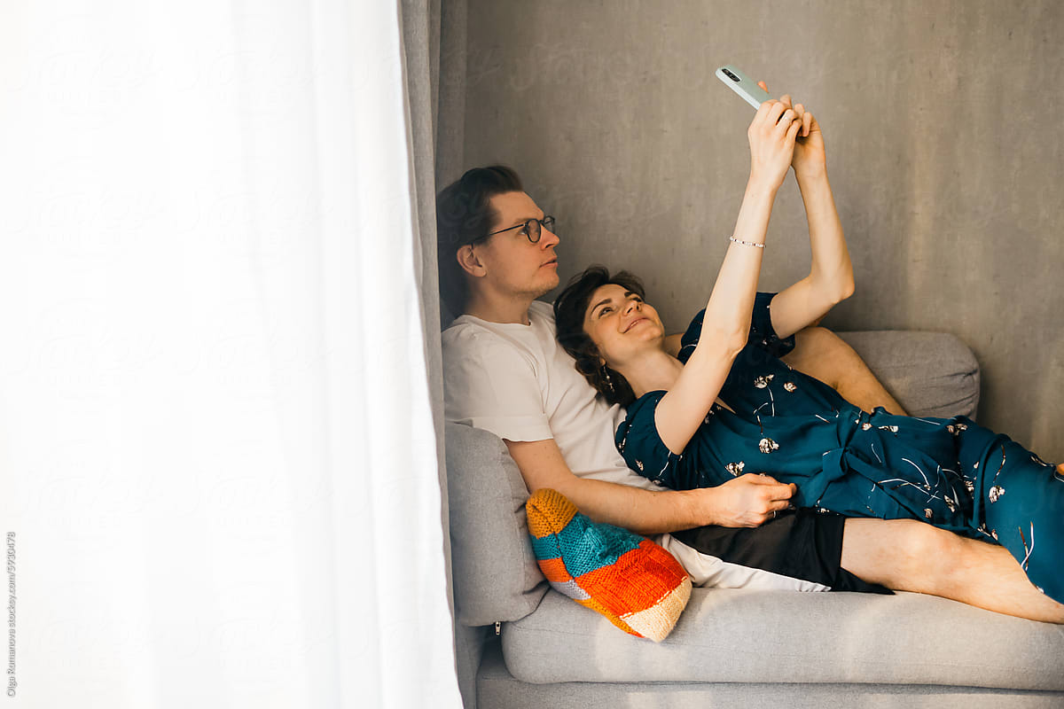 Happy couple at home on the couch making selfie with a smartphone