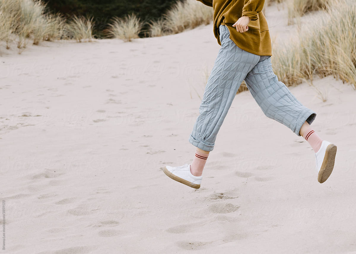 Trendy Young woman running on sand dunes wearing blue pants and white sneakers