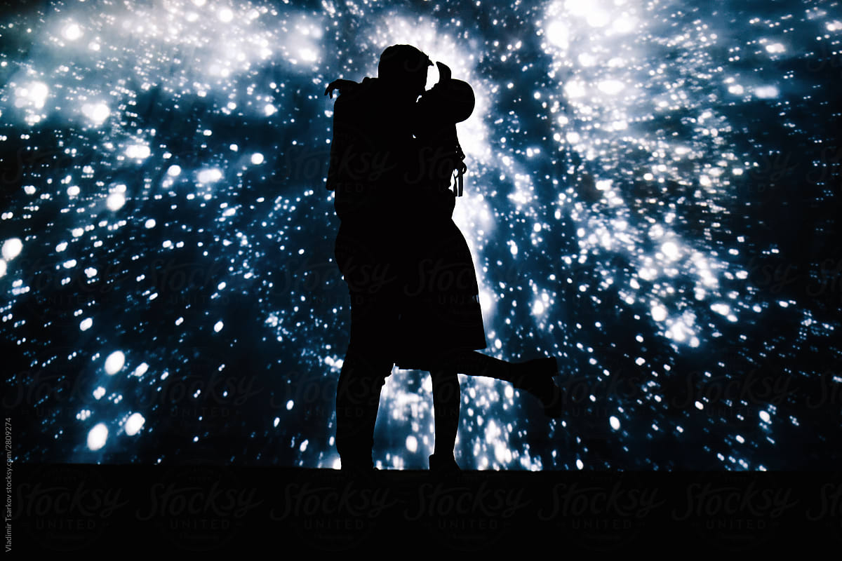 Dark silhouette of kissing couple on background with projection of starry sky
