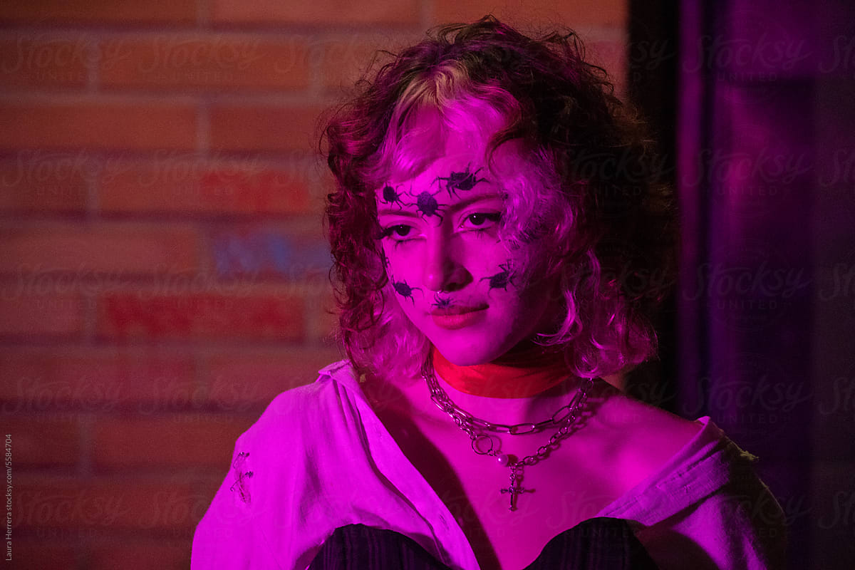 woman with spider make-up in front of brick wall with pink light