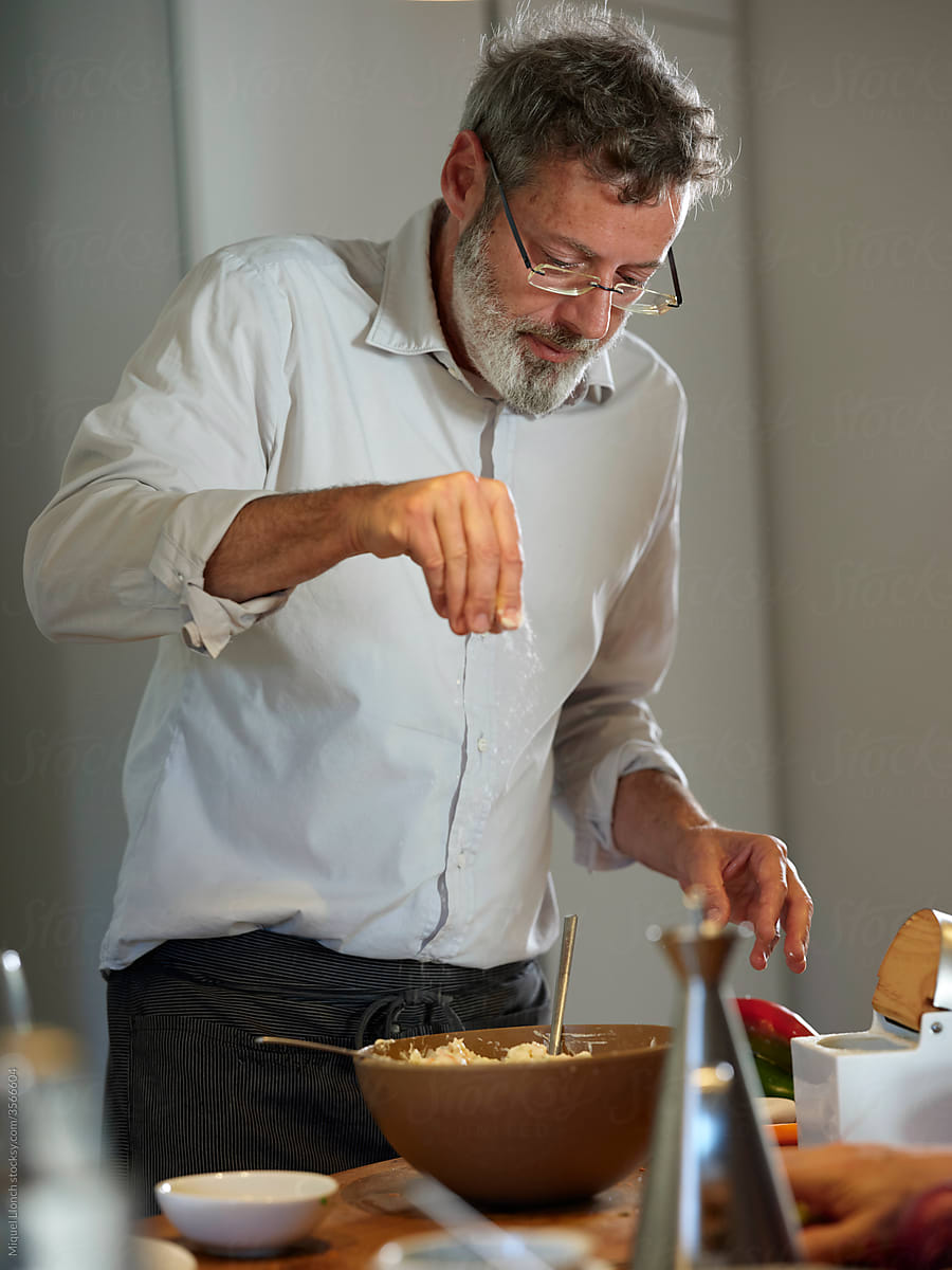 Bearded middle-aged male cook, adding salt to a salad bowl