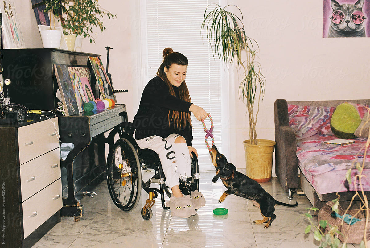 A girl in a wheelchair at home playing with her dog