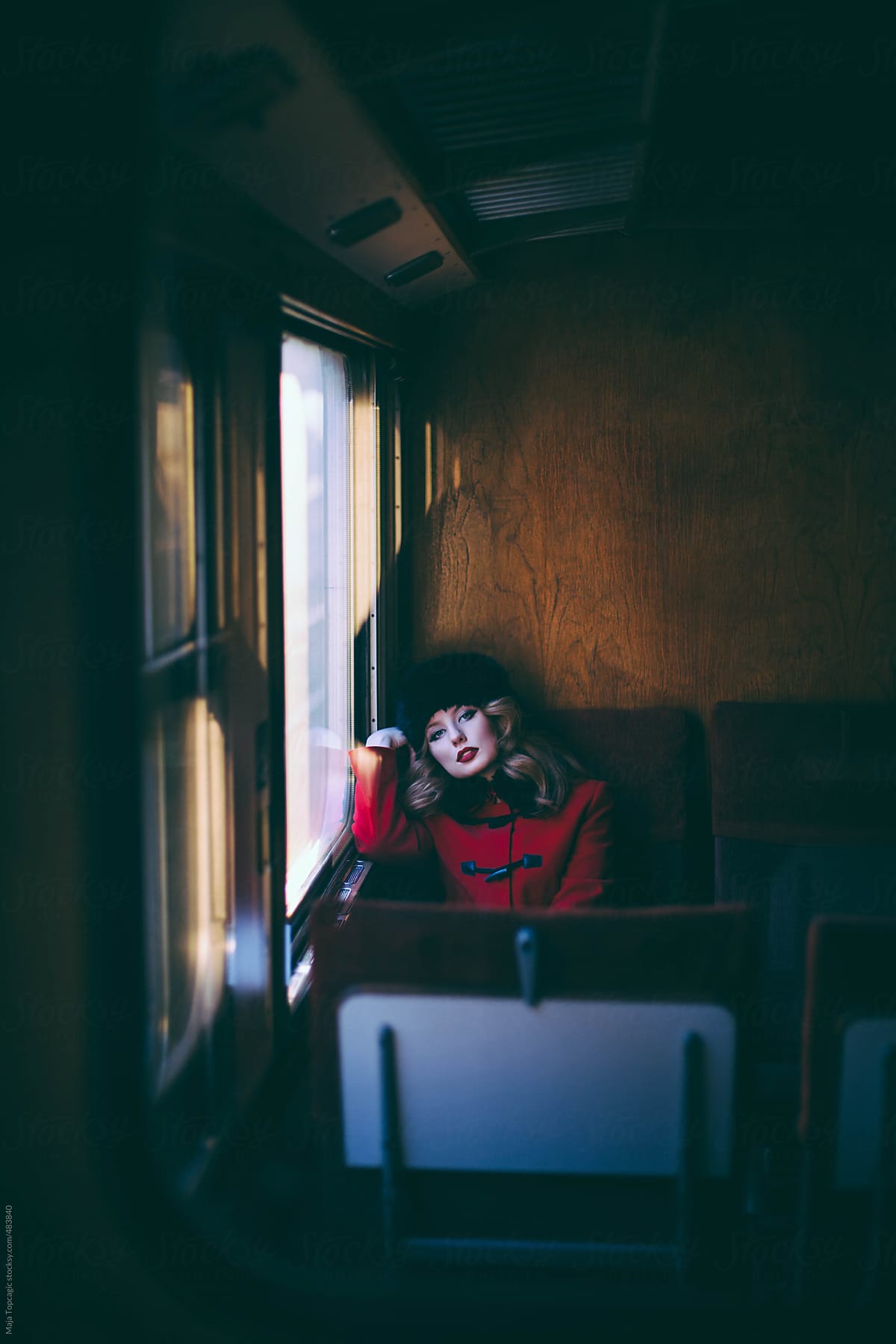 Young beautiful woman with blue eyes and curly hair in a red coat and russian fur hat in a train