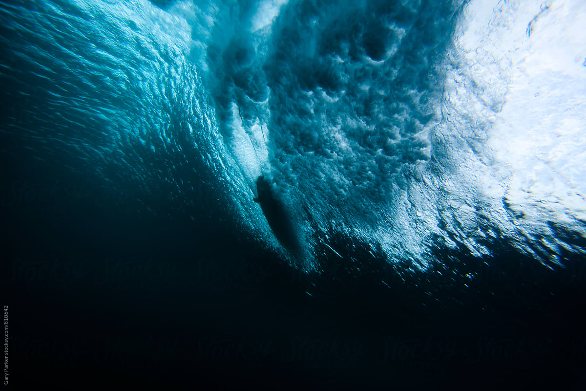 A surfboard slices through a breaking wave shot from below sea level