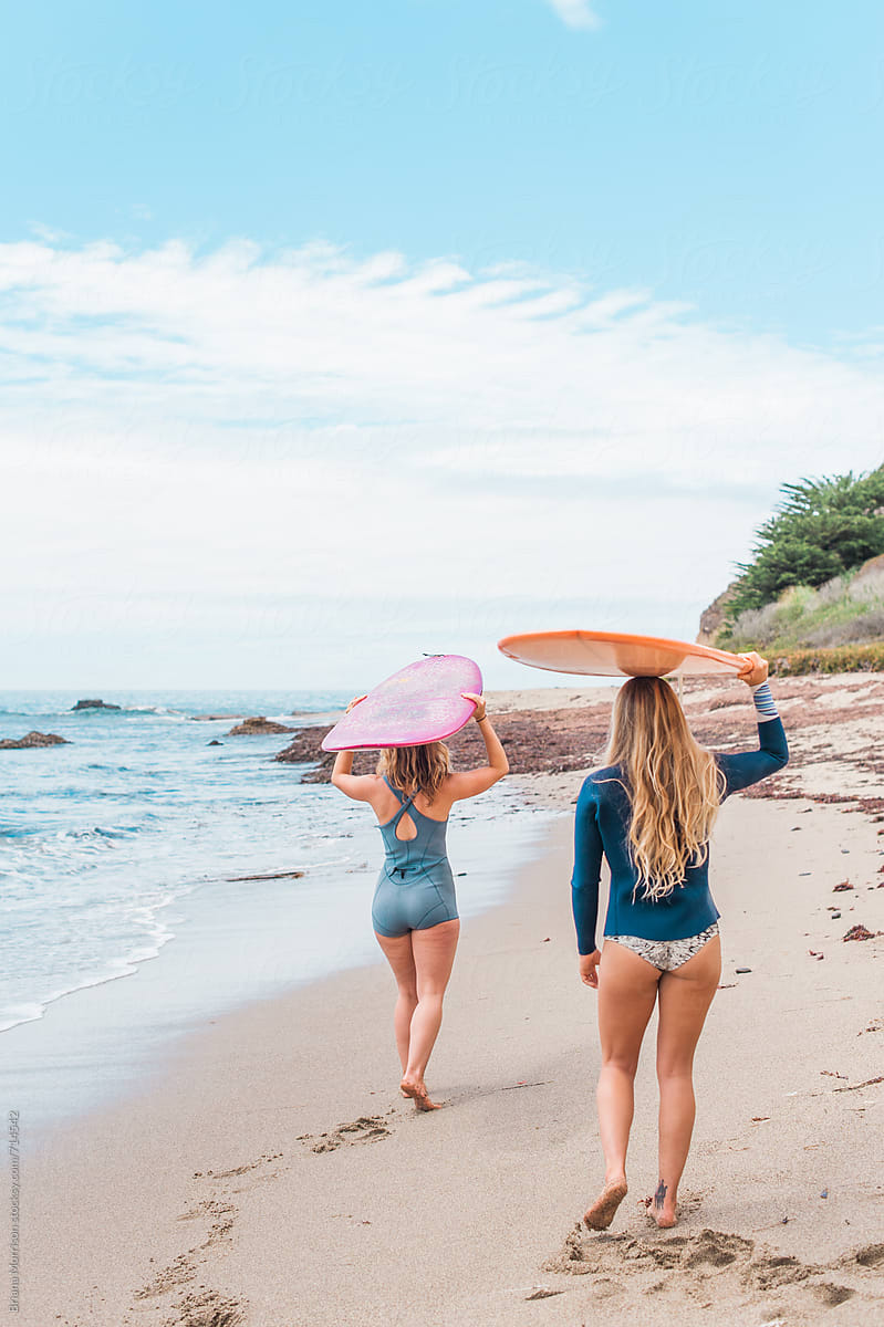 Two Women Walking On The Beach Carrying Surfboards On Their Heads