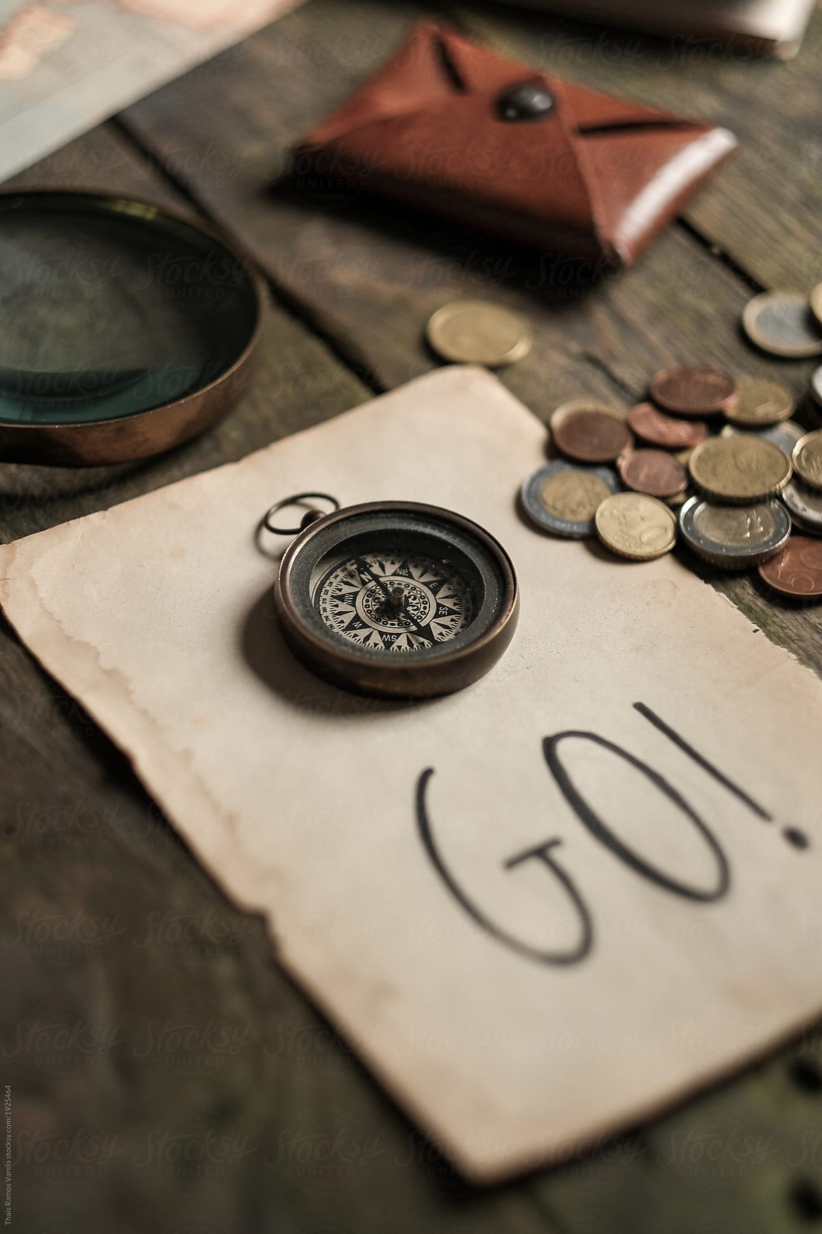 compass over a paper with go written surrounded by coins, a leather purse and a magnifying glass