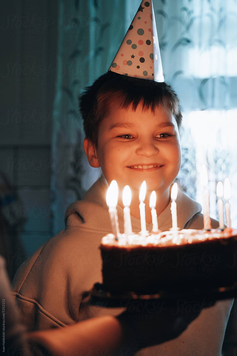 Overjoyed smiling boy with party cone blowing out candles at birthday