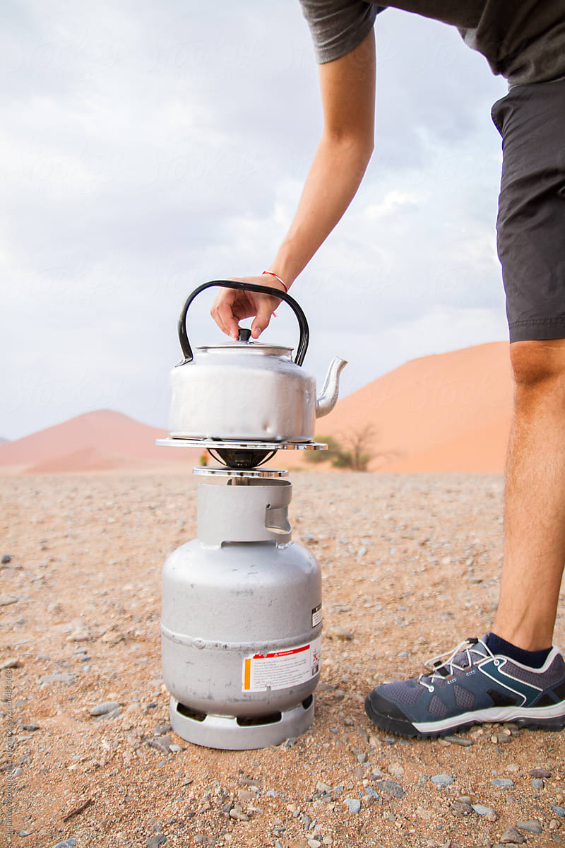 Detail of a man heating a pot of coffee on a camping gas stove gas cooker in the middle of the desert