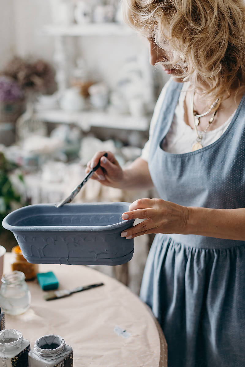 Adult woman painting pot at home