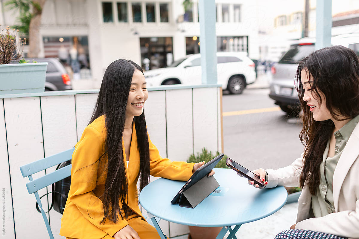 Smiling Chinese girlfriends using devices in parklet