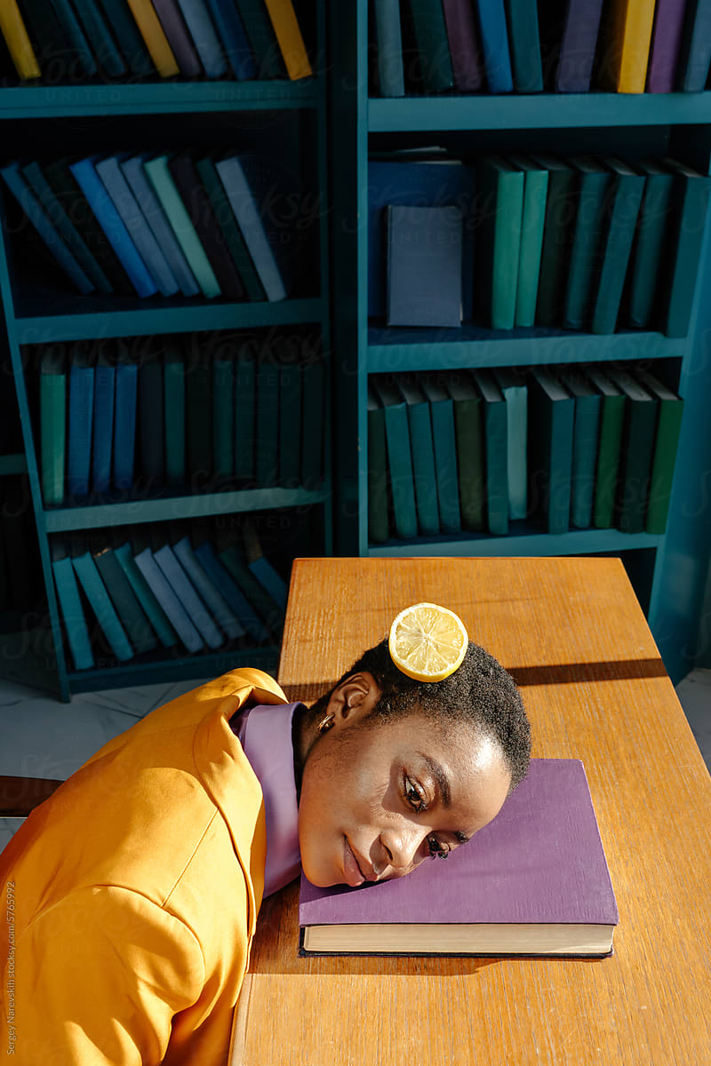 Woman with head on book, cutted lemon on hair