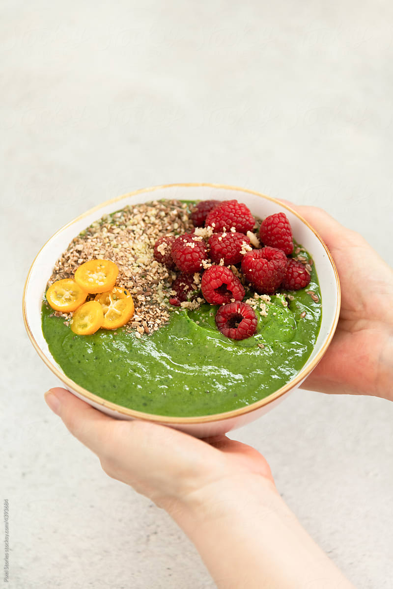 Holding spinach and kiwi detox breakfast smoothie bowl