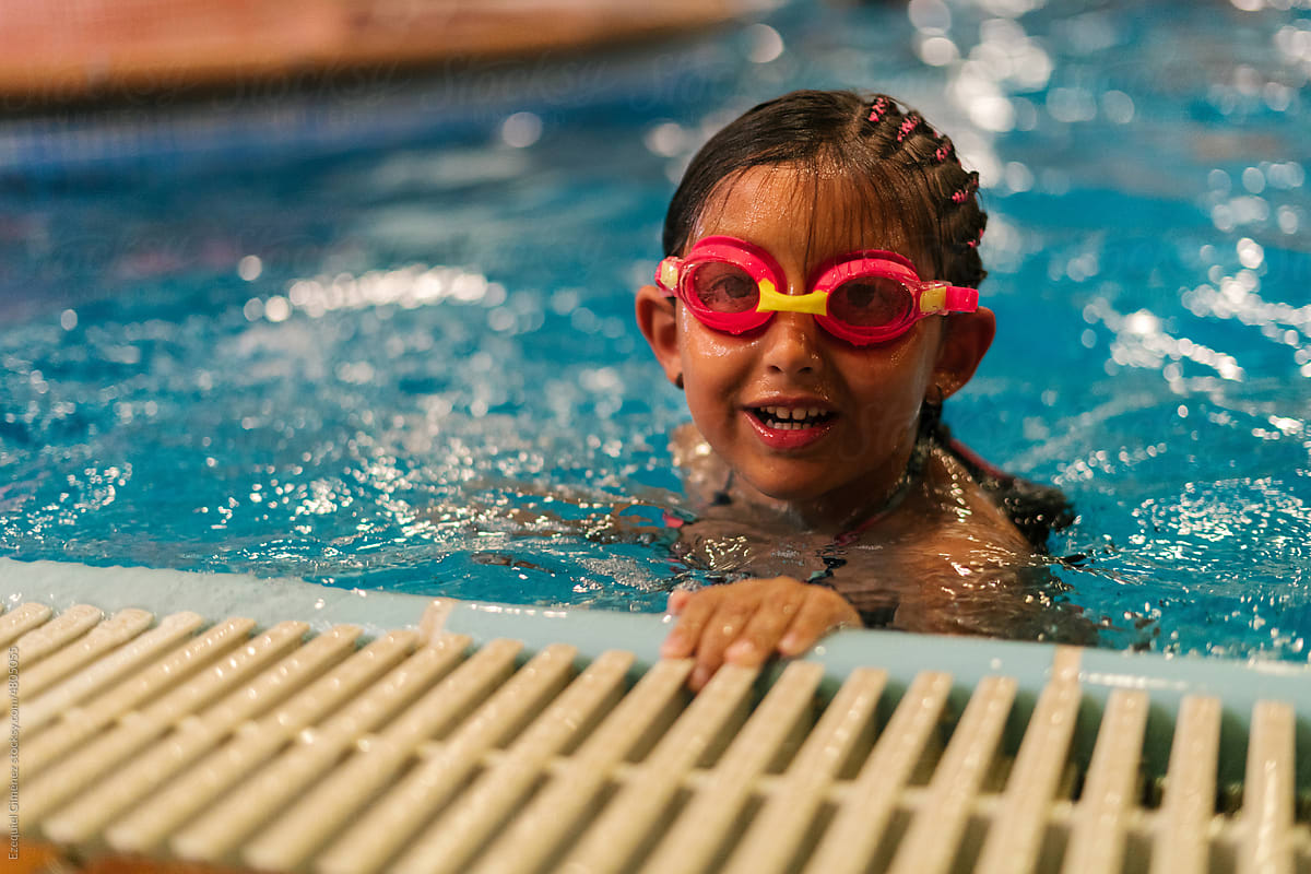 Smiling Hispanic child in goggles swimming in pool