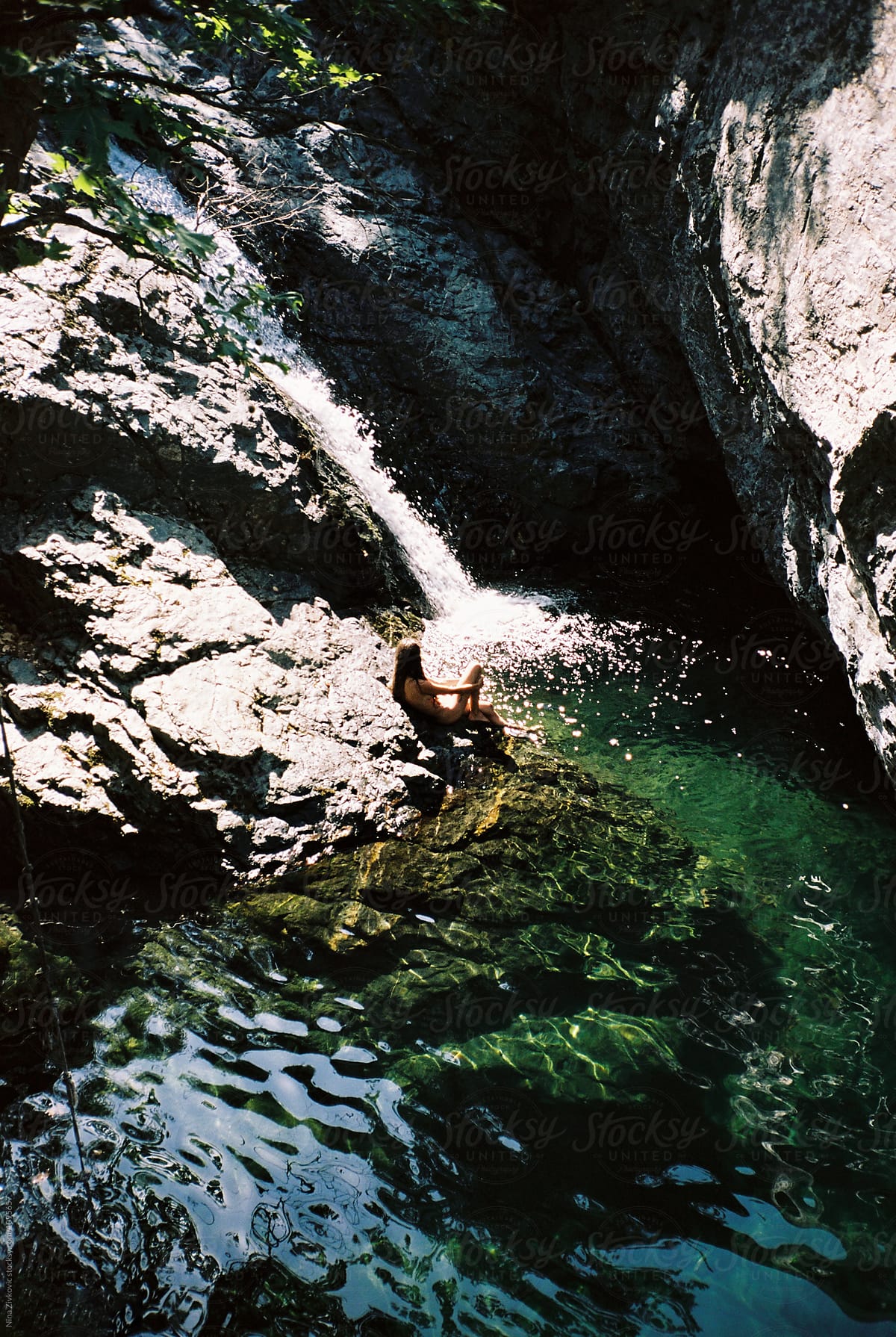 A young girl sitting by the waterfall.