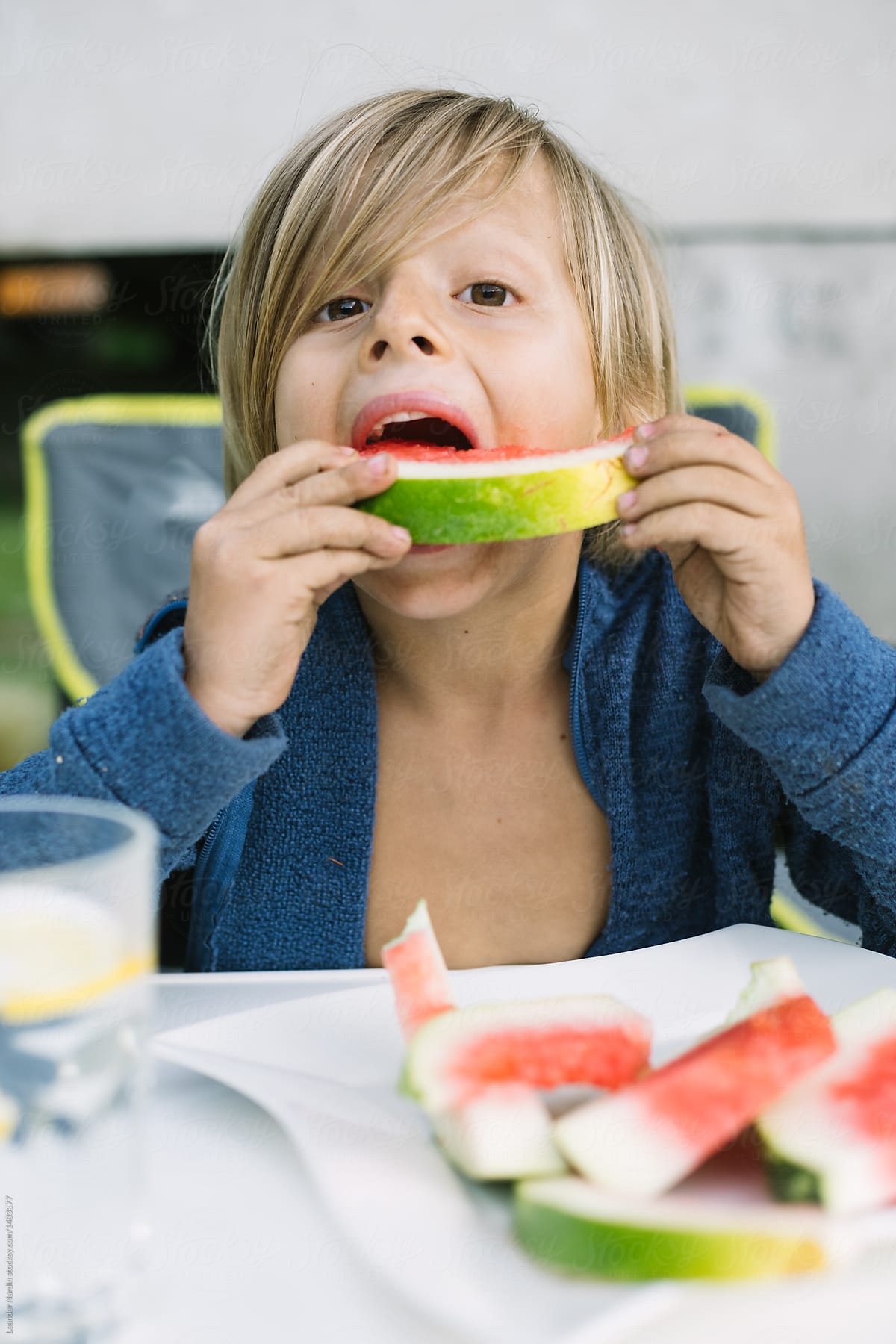 cute little toddler with long blonde hair eating water melon outdoors