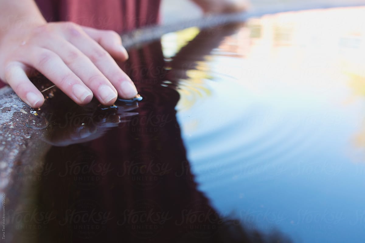 young woman\'s fingers make ripples in water fountain