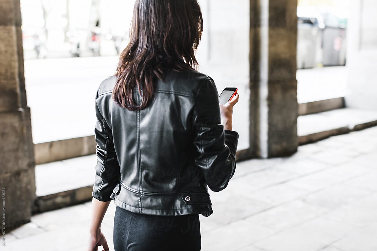 City life woman wearing leather jacket using smart phone.