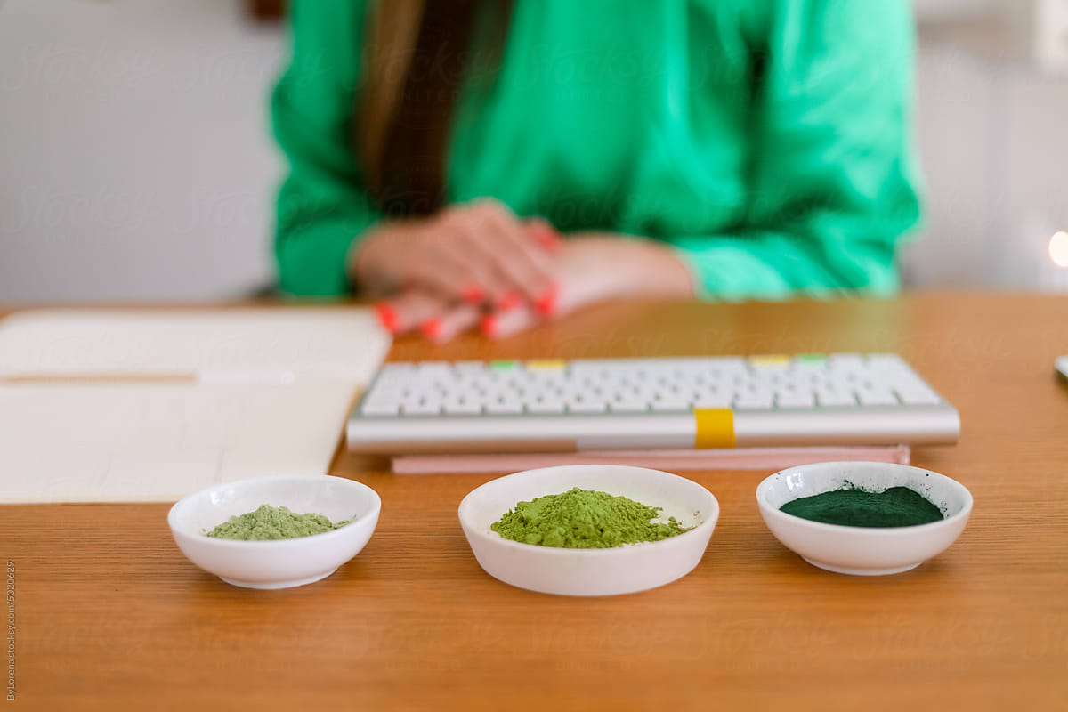 Cropped ecological dietitian at desk with powders greens
