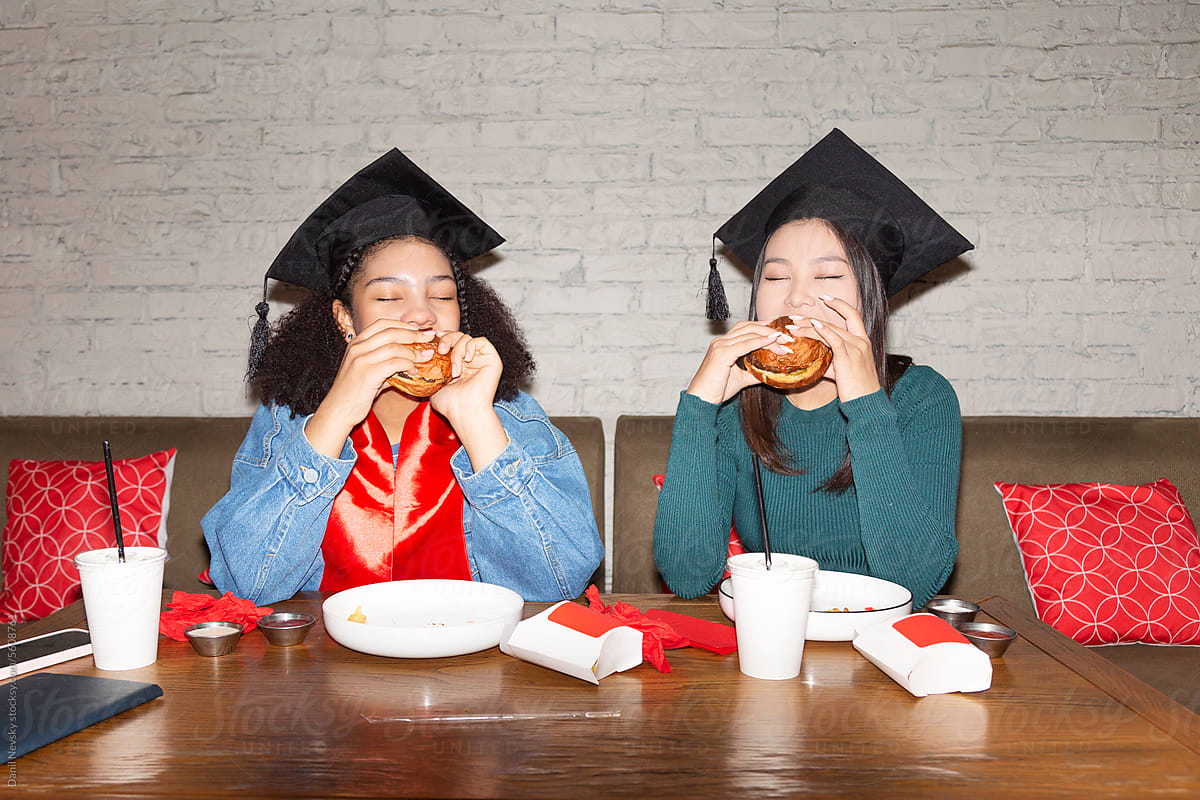 Young students eating burgers after graduation