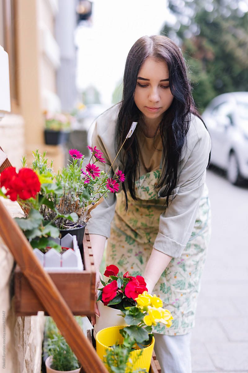 Female retailer tending about shelf with potted flowers