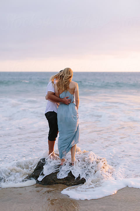 Young Couple Embracing And Spinning In Ocean Waves by Stocksy