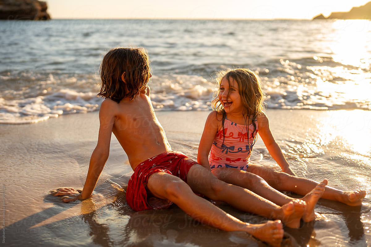 Kids sitting on the sand on an empty beach at golden time.