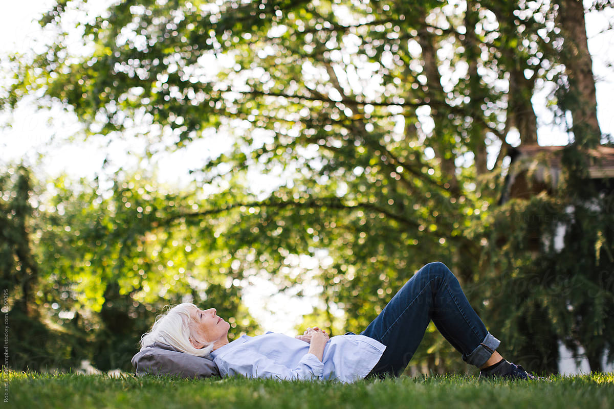Mature woman lying in the green grass looking up.