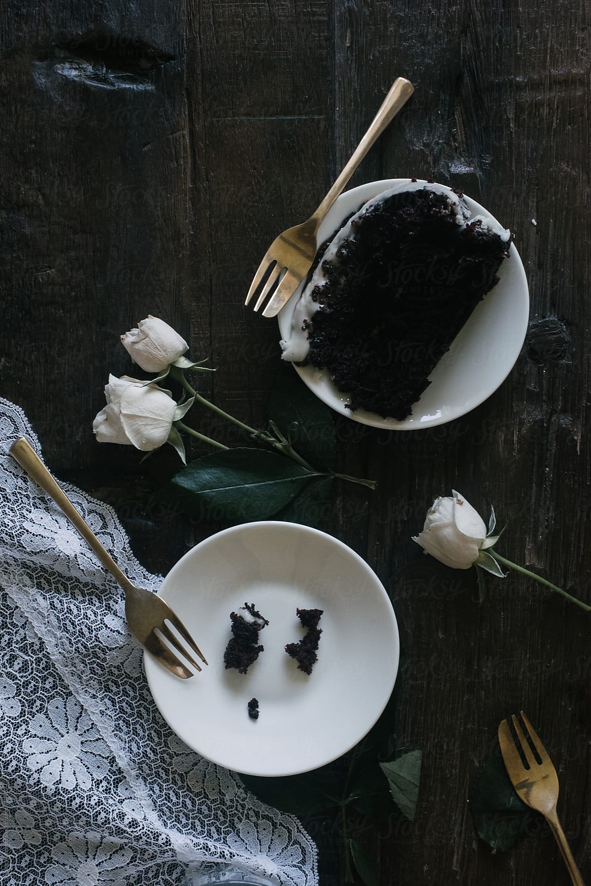Slices of chocolate cake, white mini roses and glass of milk styled on lace and dark wood table