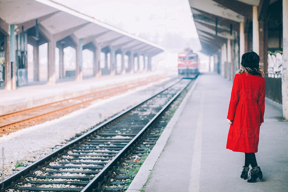 Young beautiful woman curly hair in a red coat and russian fur hat on a train station