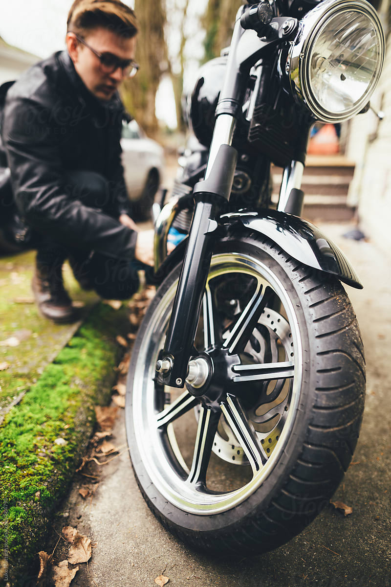 Young Man In Leather Jacket Polishing Black Motorcycle In Driveway