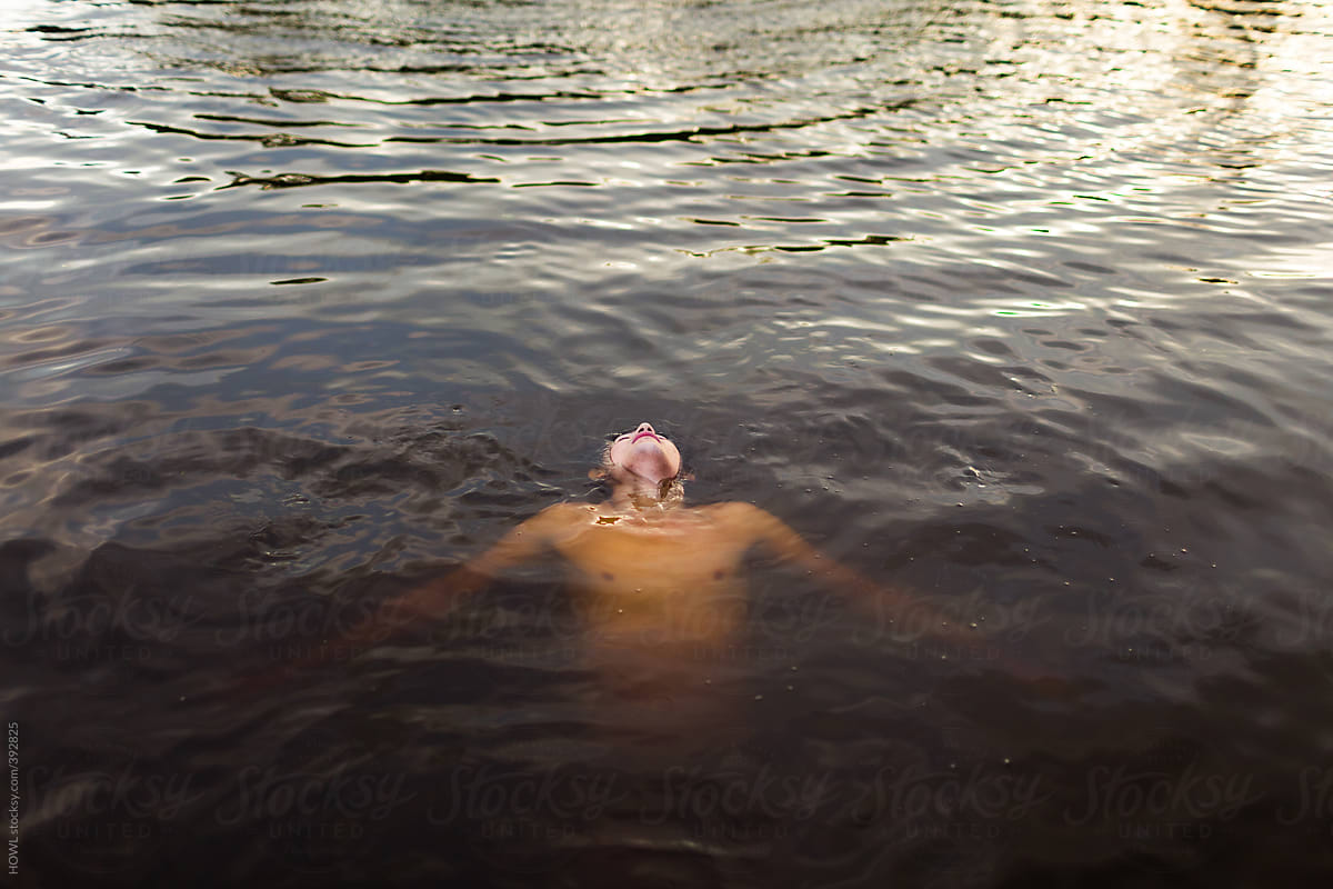 A young man floats on his back in a lake on a summer day