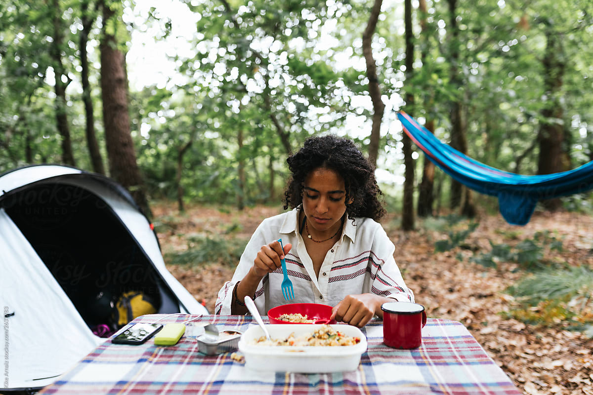 African american woman eating some food, A tent and a blue hammock background.