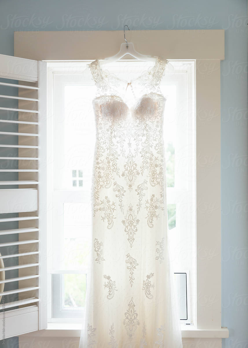 A beautiful wedding dress, hung by a window
