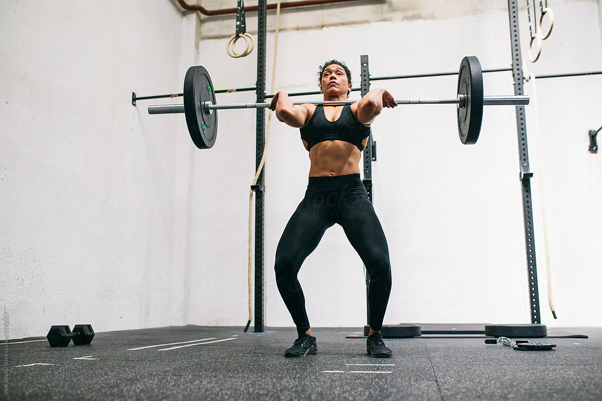 Hispanic female weightlifter squatting with barbell