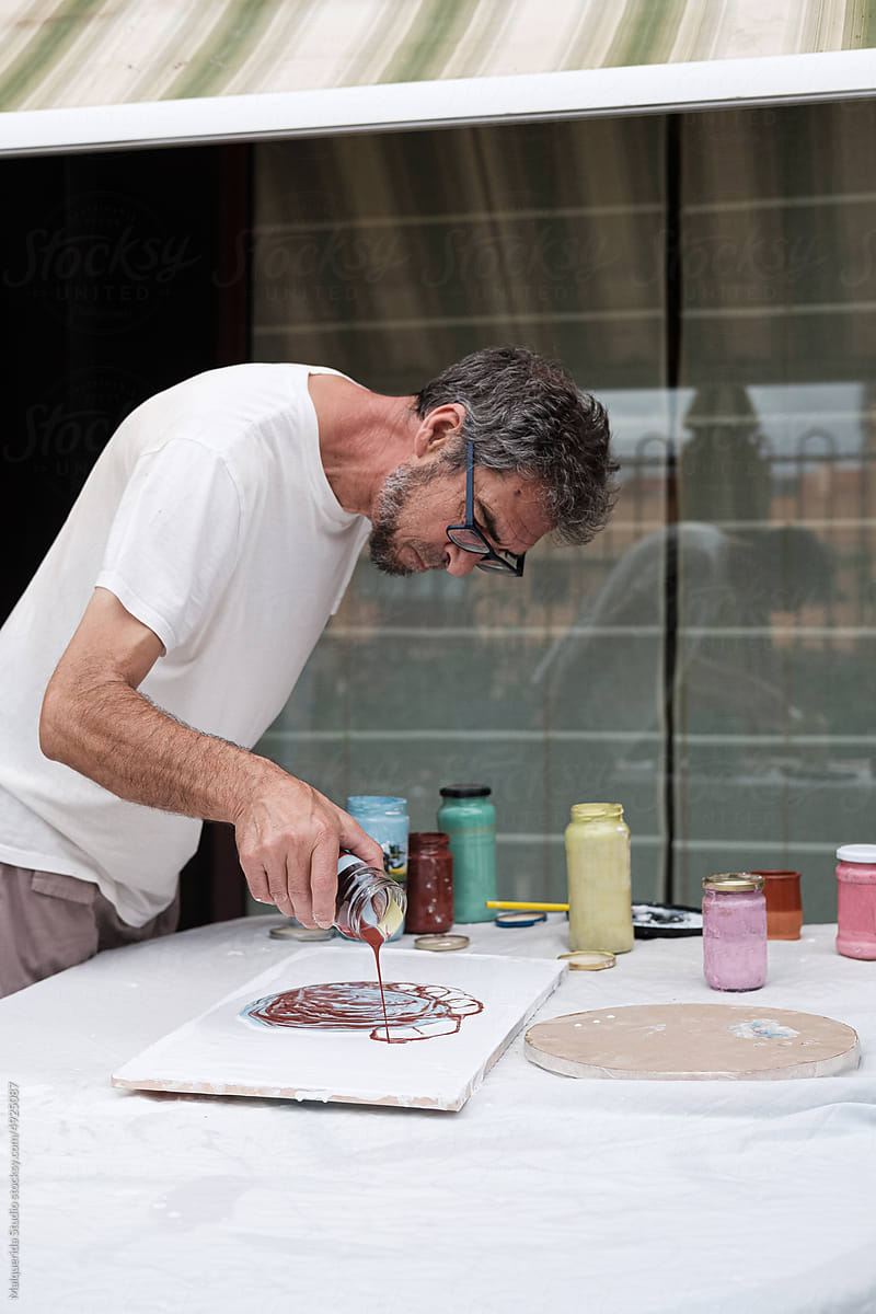 Mature artist pouring colorful paint